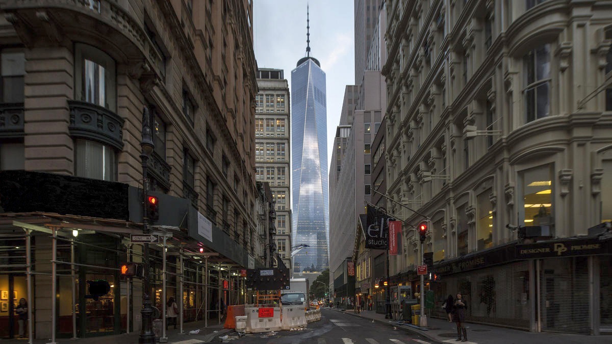 one world trade center seen down at the end of a street, between older buildings. there is construction going on in the foreground